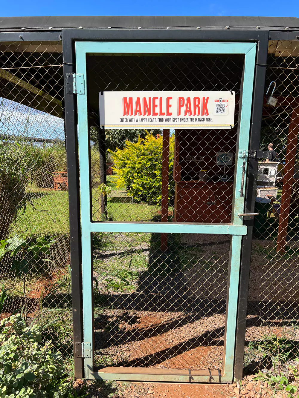 Entrance gate to the Lāna‘i Cat Sanctuary at Mānele Park, featuring rustic fencing, welcoming signage, and tropical greenery in the background.