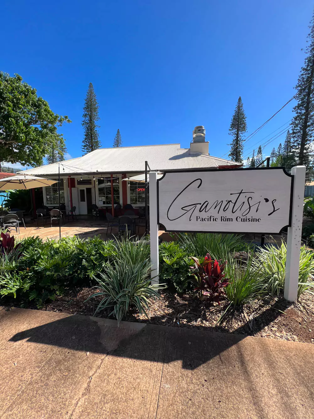 Exterior of Ganotisi’s Pacific Rim Cuisine on Lāna‘i, featuring colorful trim, and tropical plants out front.