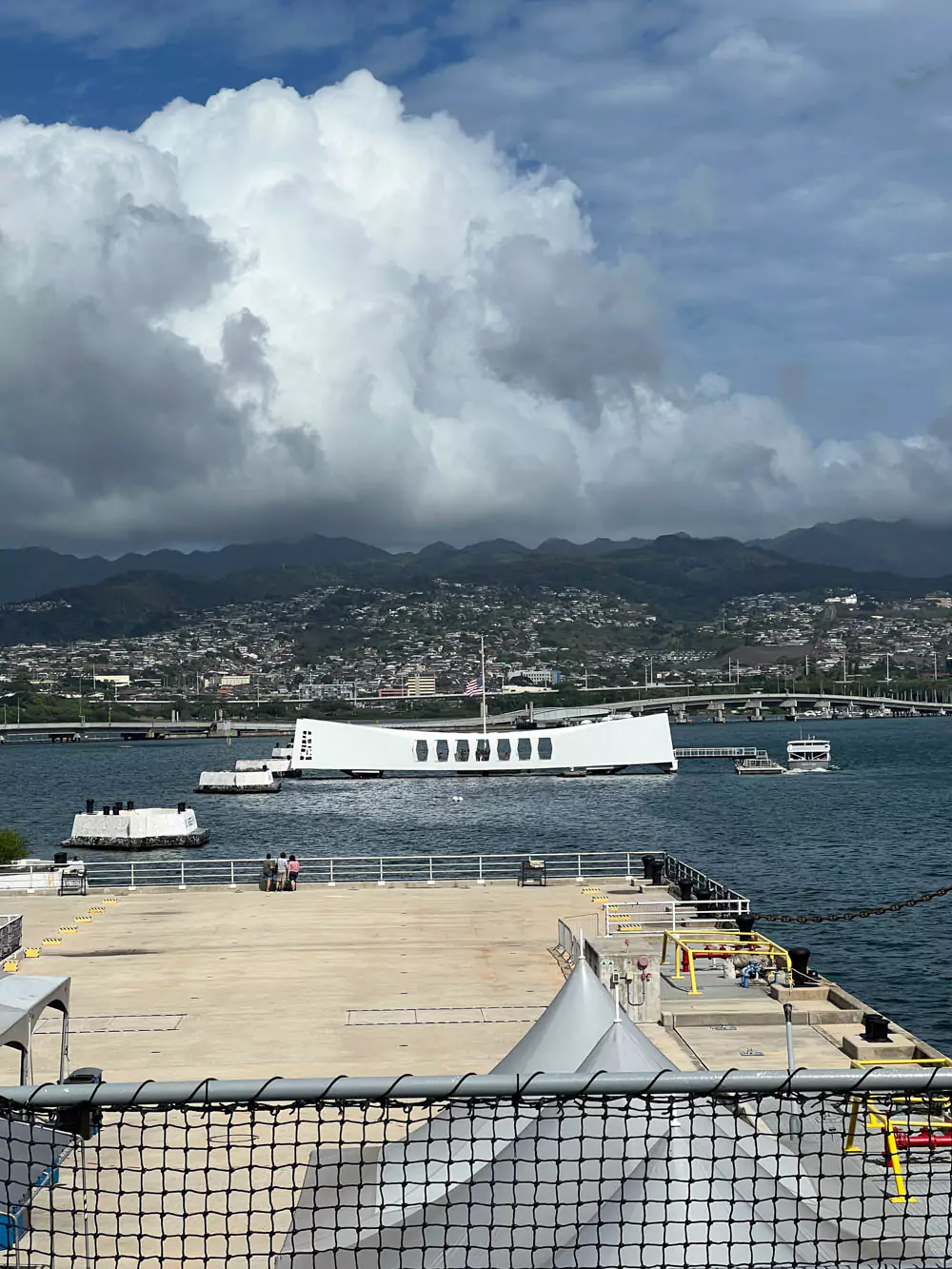 USS Arizona Memorial in Pearl Harbor, a white structure spanning the sunken battleship, honoring the lives lost during the 1941 attack, with flags flying above and reflections on the water below.