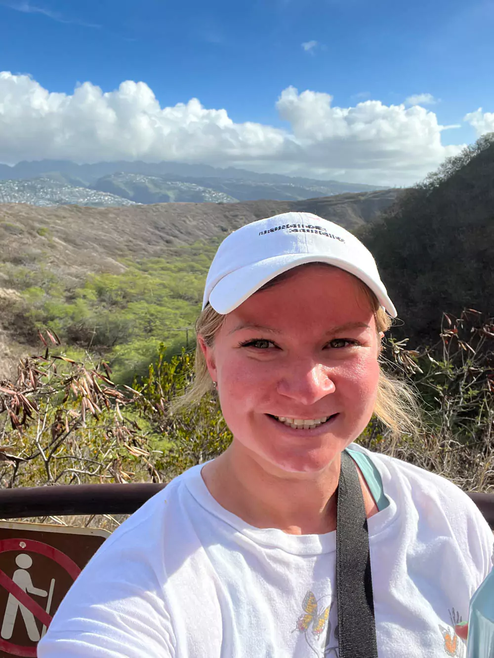 Katie taking a selfie at the edge of Diamond Head crater, with panoramic views of the volcanic landscape, Honolulu skyline, and Pacific Ocean behind her.