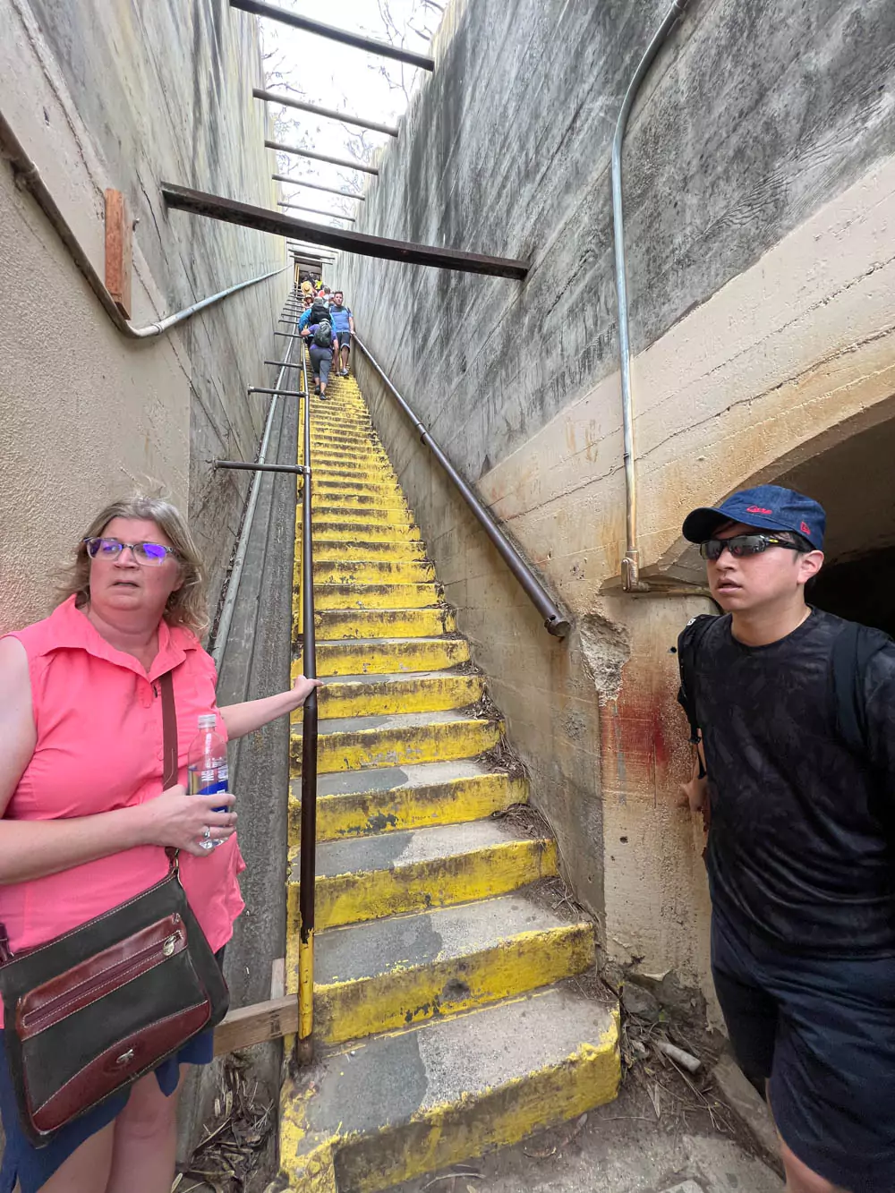 Barb standing at the bottom of the steep staircase on the Diamond Head trail, looking up toward the challenging ascent with crater walls surrounding her.