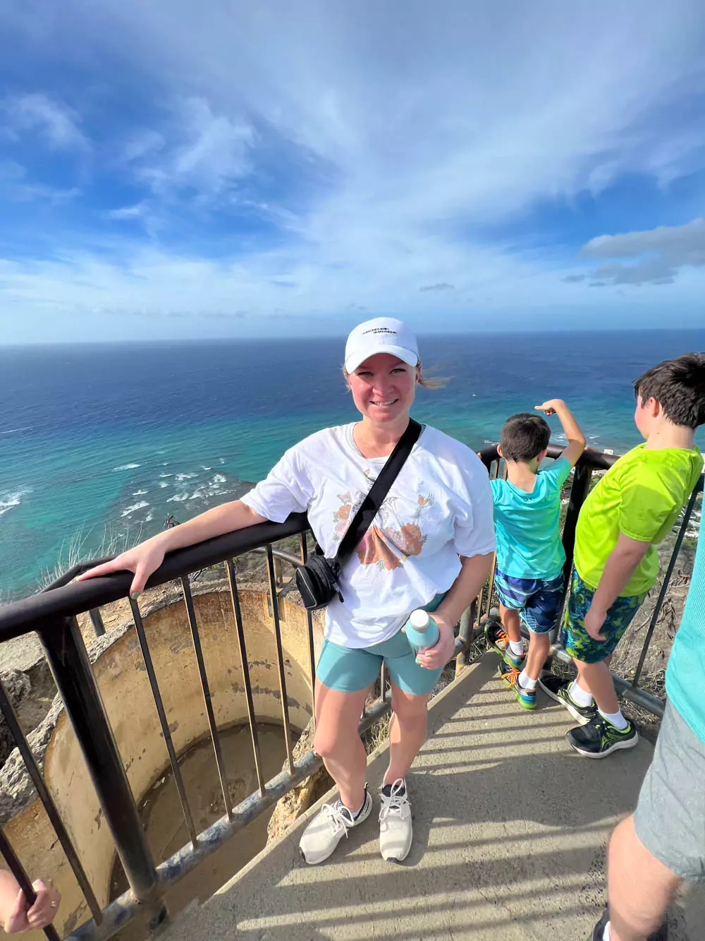 Katie standing at the summit of Diamond Head State Monument, smiling with sweeping views of Honolulu, the Pacific Ocean, and the crater rim behind her.