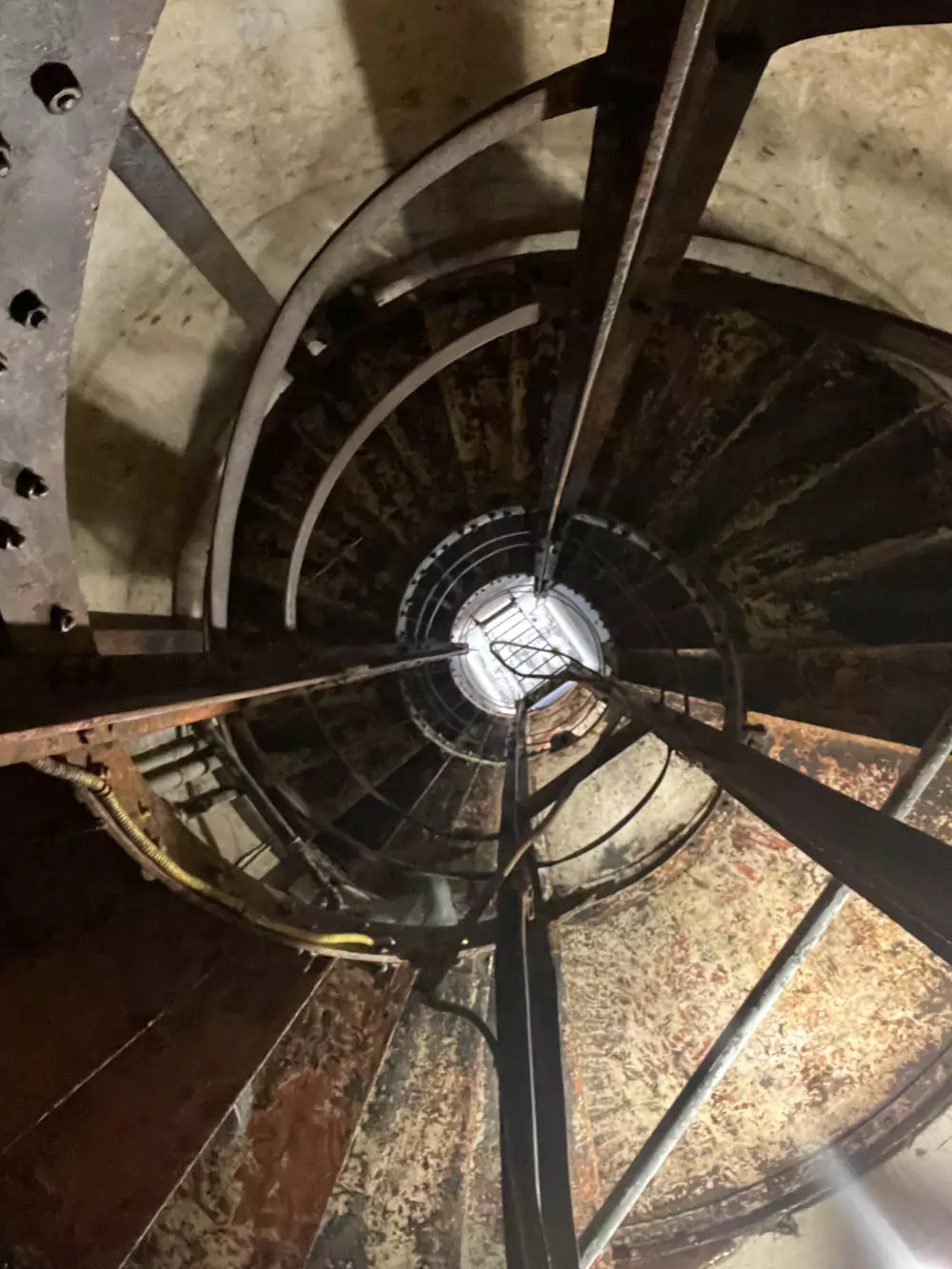 View looking down the narrow spiral staircase inside the Diamond Head pillbox, with worn metal steps and dim light leading into the historic World War II bunker.