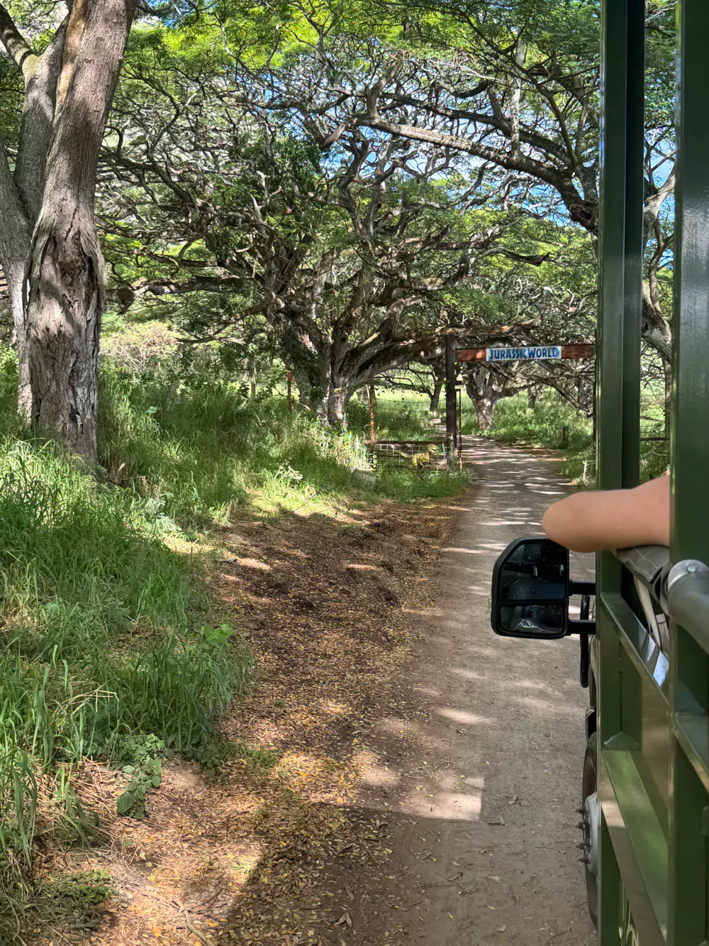 riginal Jurassic Park gates filming location at Kualoa Ranch in Oʻahu, Hawaii, showing vehicle-sized gateposts along a dirt road, set against a lush jungle and mountain backdrop.
