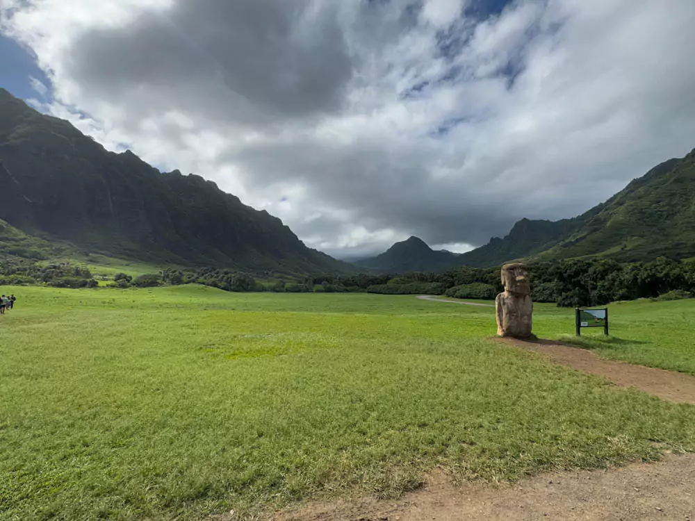 Filming location for Mystery of Easter Island at Kualoa Ranch, featuring an open grassy plain surrounded by dramatic green cliffs and jungle, resembling the isolated island setting.