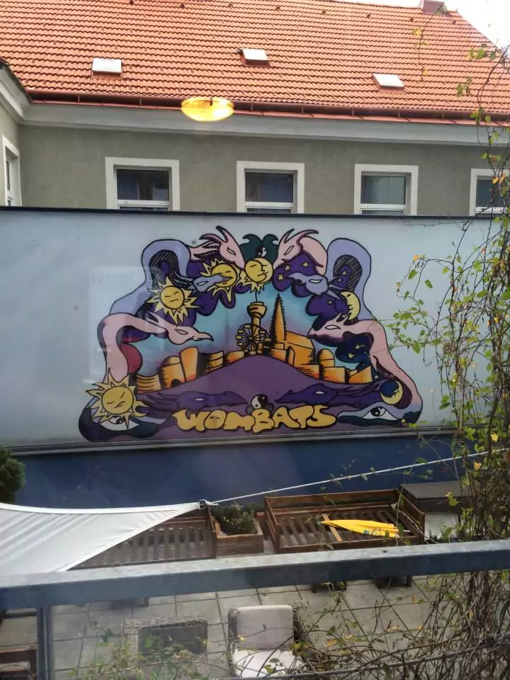 A colorful mural decorates the courtyard wall of Wombats Hostel in Vienna, featuring vibrant street art with playful characters and bold designs. The lively artwork adds a creative, urban vibe to the hostel’s communal outdoor space.