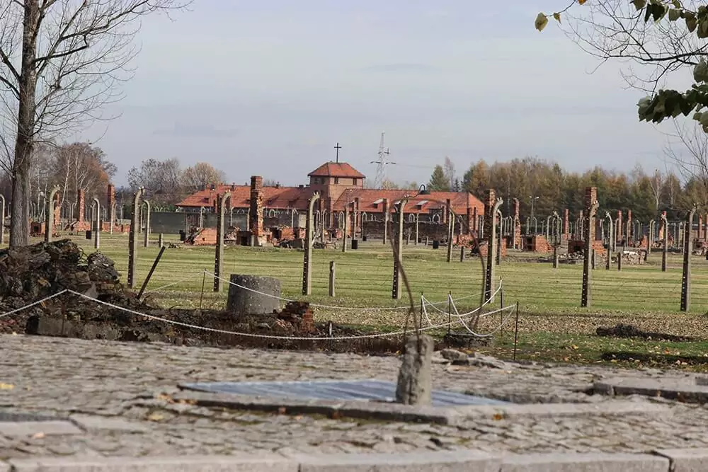 The somber ruins of Birkenau, part of the Auschwitz-Birkenau concentration camp, showing crumbling brick buildings and desolate grounds under a gray sky. The site serves as a powerful reminder of the Holocaust’s history.