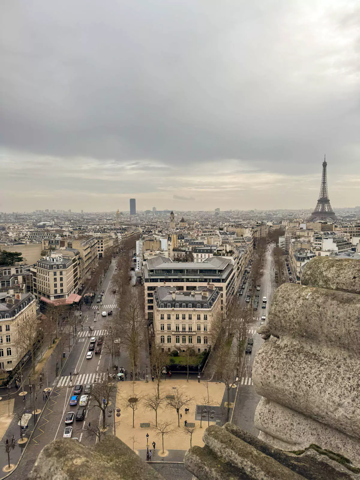 Breathtaking view from the top of the Arc de Triomphe in Paris, France, looking toward the Eiffel Tower rising above the city’s rooftops, with Haussmann-style buildings and tree-lined avenues in the foreground.