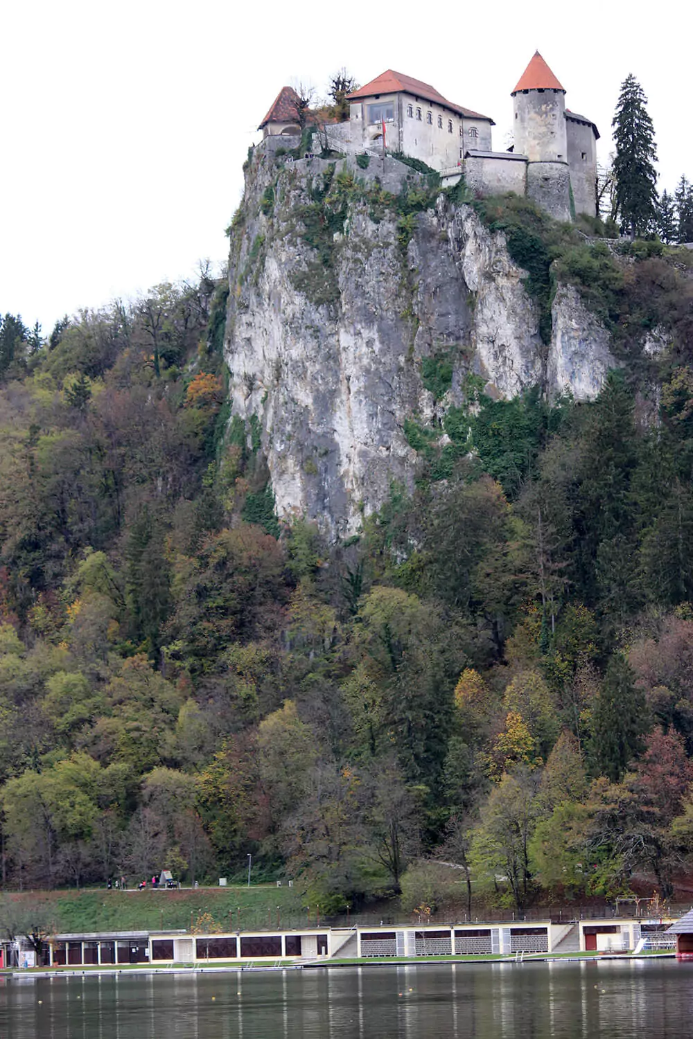 Scenic view of Lake Bled in Slovenia with the medieval Bled Castle perched on a cliff overlooking the turquoise water. The serene lake is surrounded by lush green hills under a clear sky.