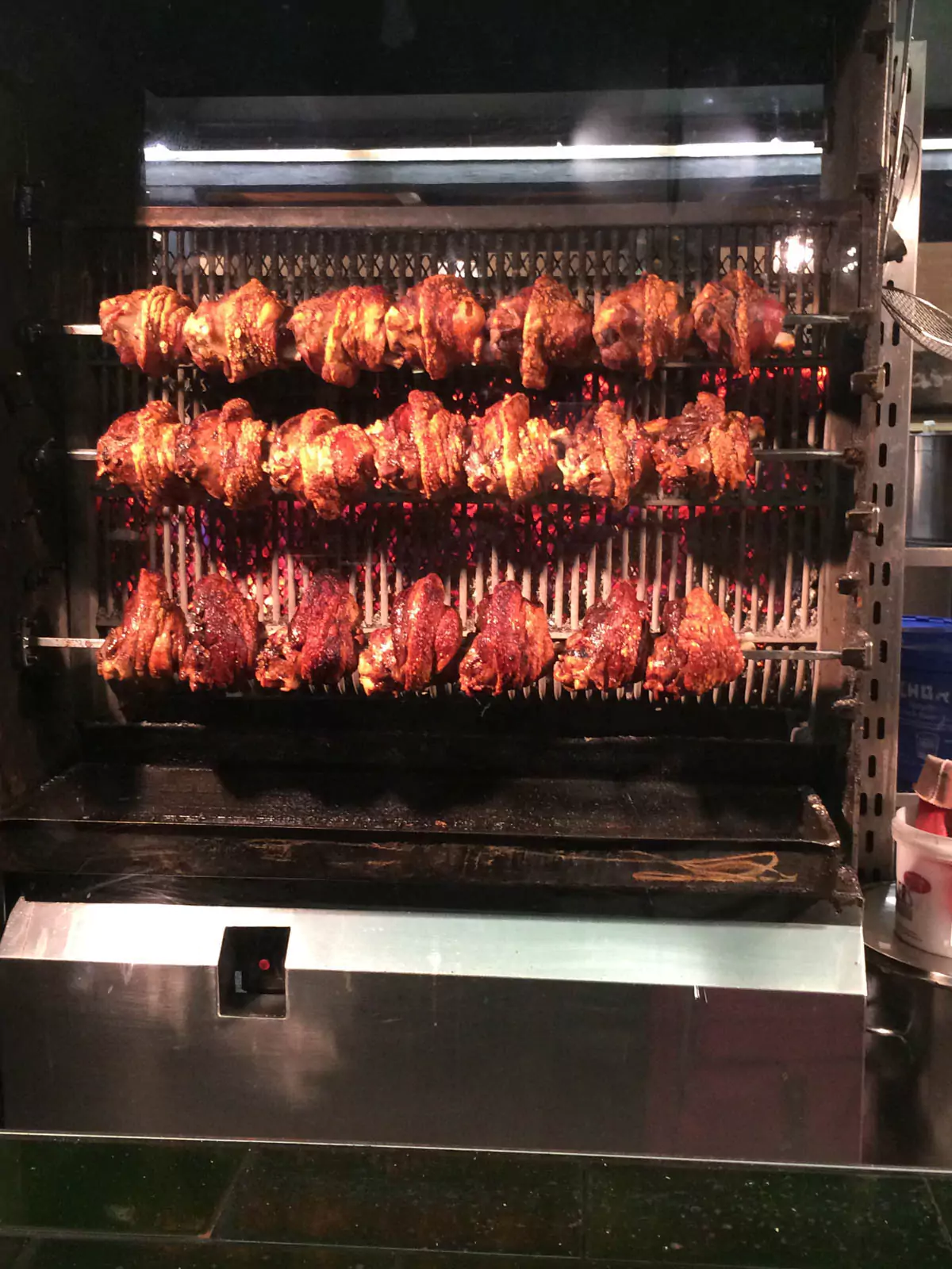 A crispy pork knuckle (schweinshaxe) roasting on a rotating spit inside a restaurant window, with golden-brown skin and visible juices. The savory dish is showcased to entice passersby with its traditional Bavarian flavor.