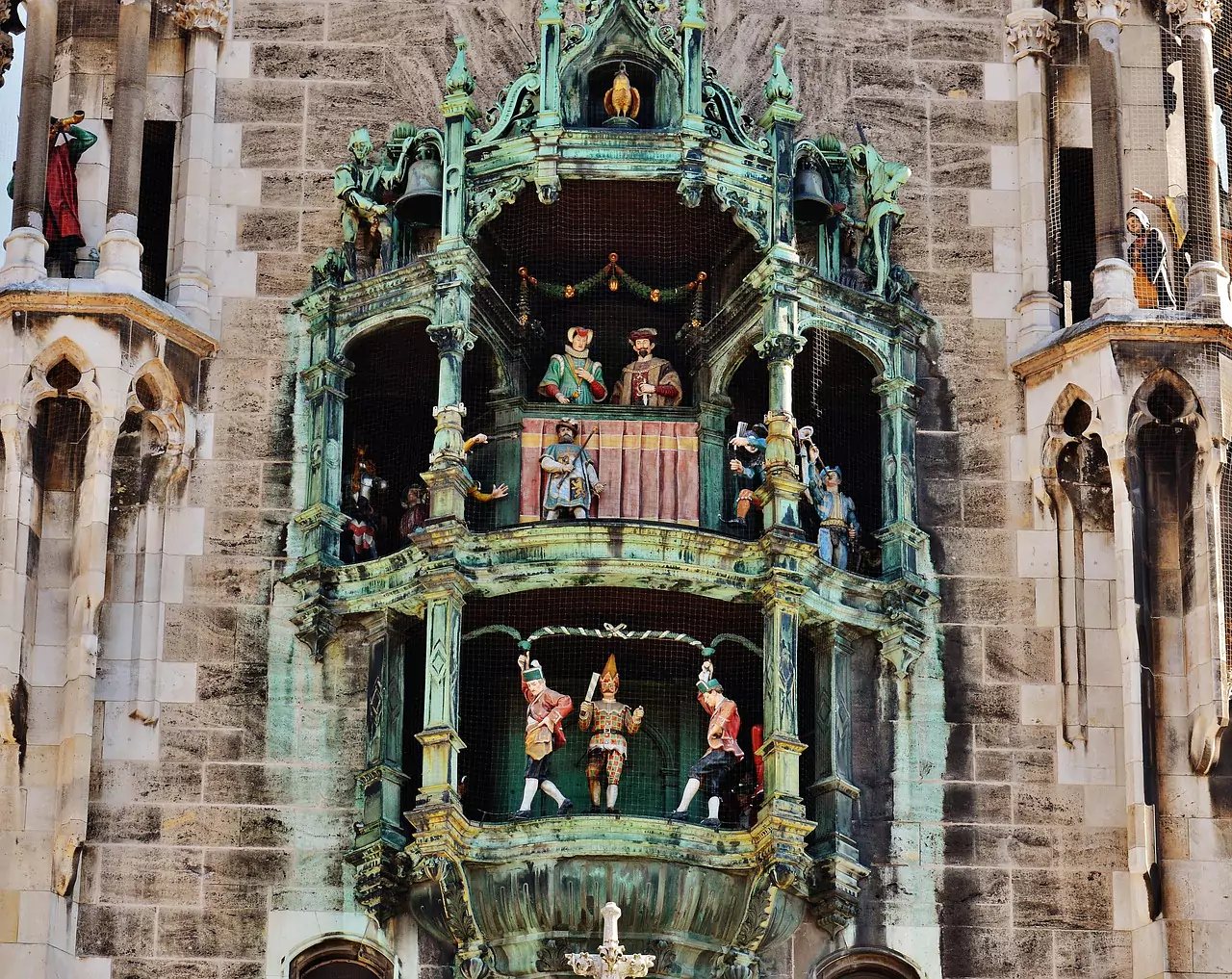 The ornate Gothic Revival facade of Munich Town Hall, featuring detailed stone carvings, tall spires, and a large clock tower. The historic building stands prominently on Marienplatz in the heart of Munich.