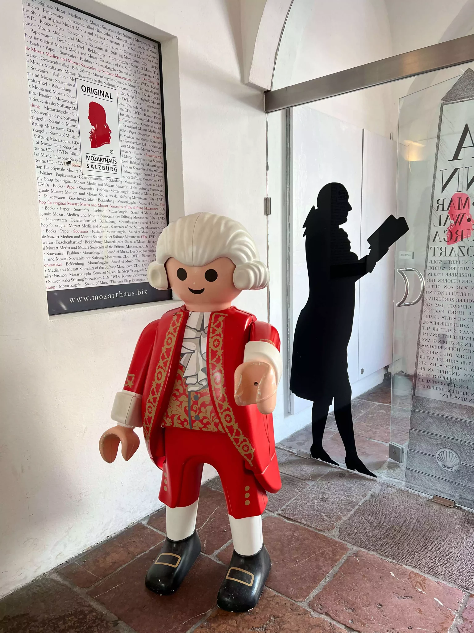A cartoonish statue of Mozart stands playfully at the entrance of the Mozart Residence in Salzburg, Austria. With exaggerated features and a whimsical pose, the statue adds a lighthearted twist to the historic setting.