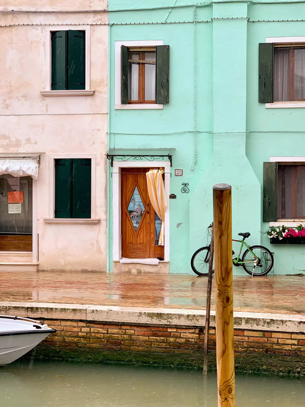 A wooden door with stained glass panels featuring pink flamingos stands out on a teal-colored house in Burano, Italy. The playful glass art adds a tropical flair to the already vibrant and whimsical island aesthetic.
