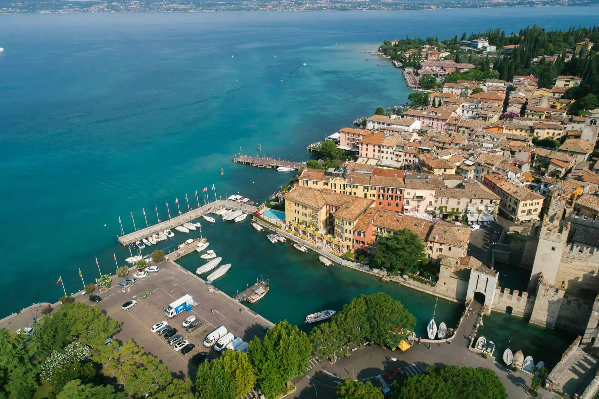 Aerial view of Lake Garda in Italy, showing the expansive blue lake surrounded by mountains, terraced villages, and lush green hills, with boats scattered across the water.