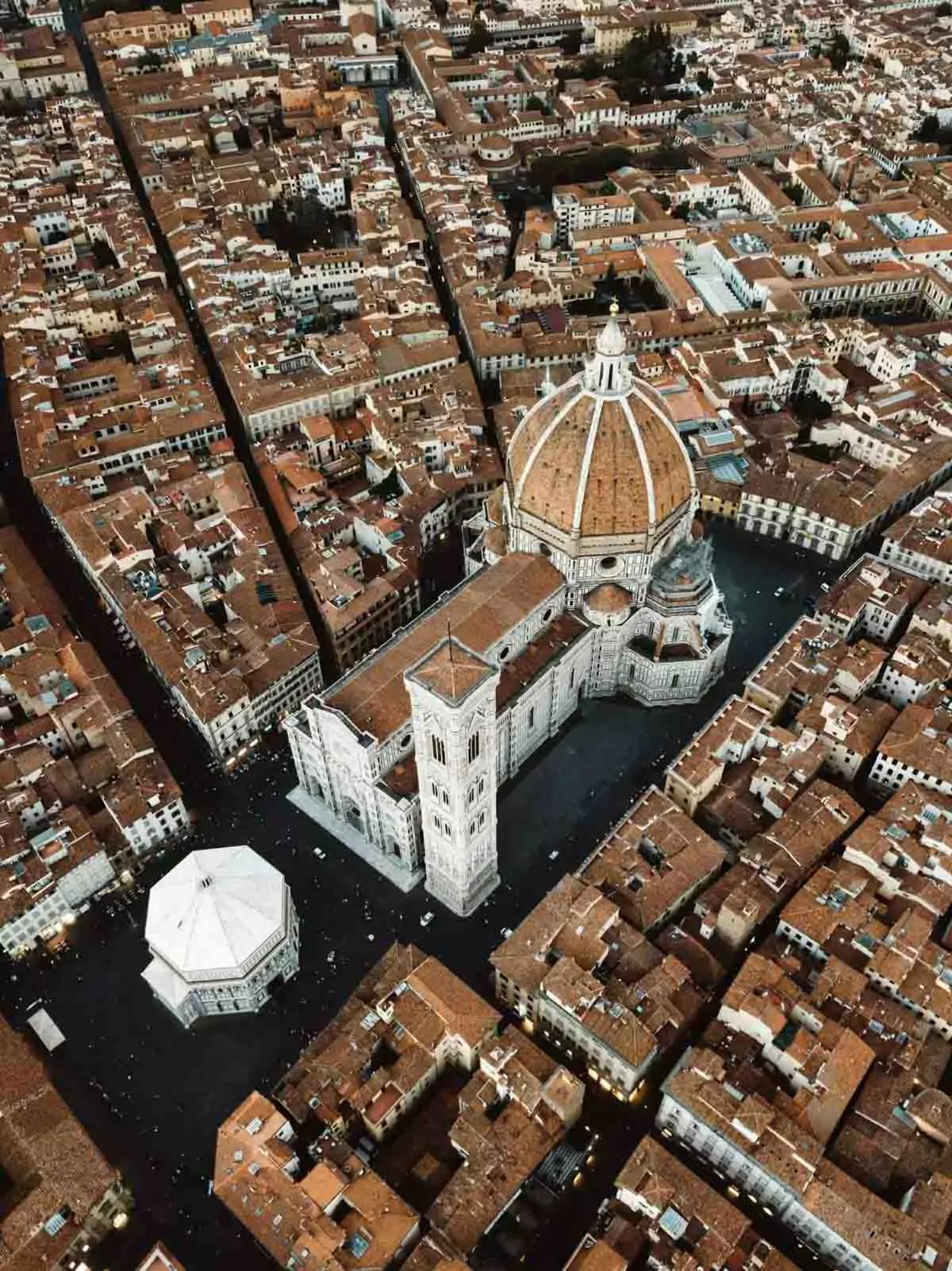Aerial view of the Cupola del Brunelleschi, the iconic red-tiled dome of Florence Cathedral, rising above the historic cityscape of Florence, Italy, with terracotta rooftops and Tuscan hills in the distance.