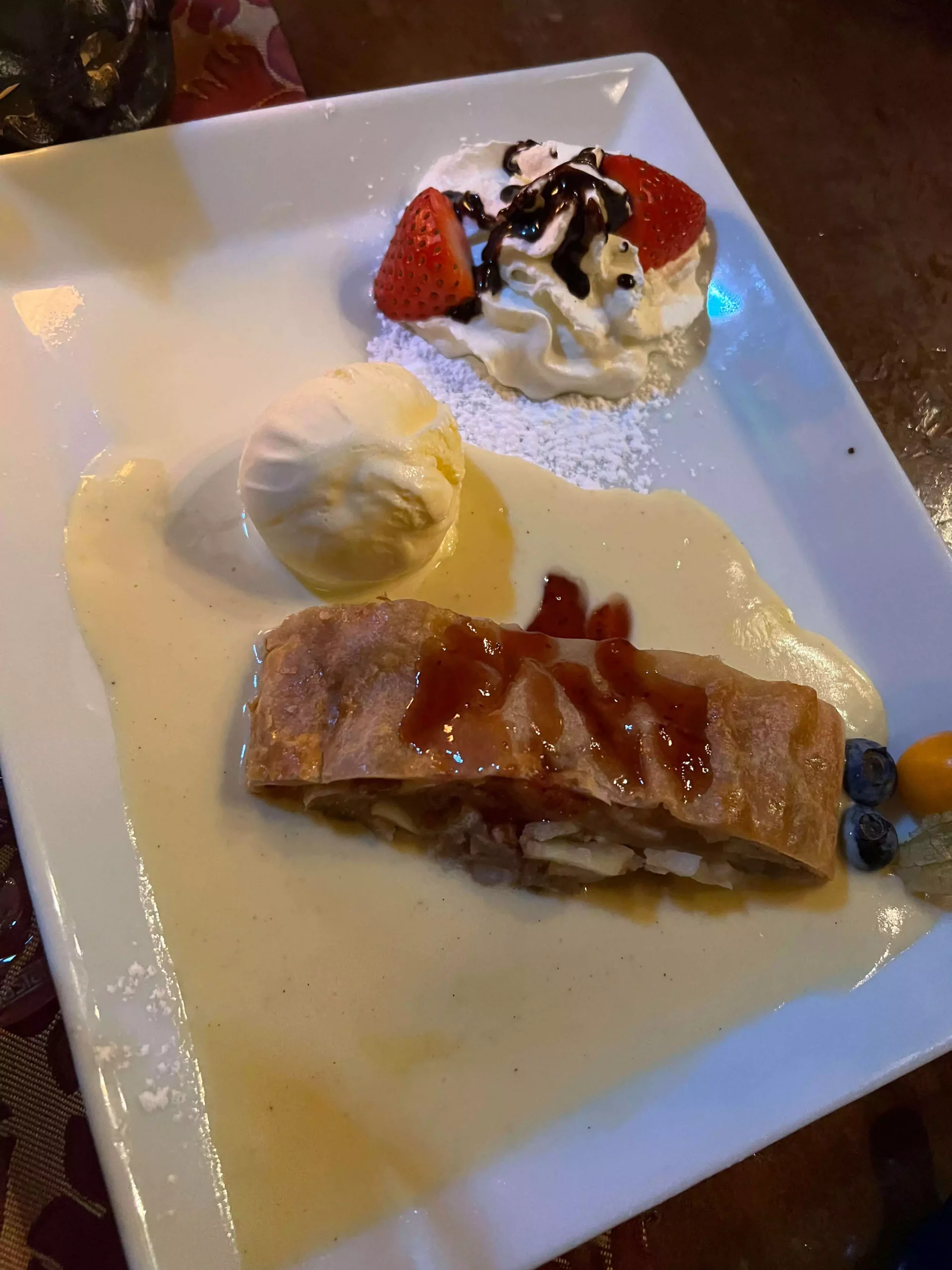 A plate of apple strudel served at Im Keller in Nuremberg, Germany, topped with powdered sugar and a scoop of vanilla ice cream slowly melting beside it. The golden, flaky pastry reveals a spiced apple filling, capturing the essence of a classic German dessert.