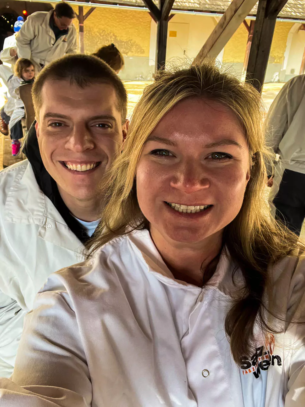 Katie and Zack inside Hallstatt Salt Mine (Salzwelten), dressed in white miner outfits and smiling as they stand together in one of the dimly lit underground tunnels. The rocky salt walls and historic setting highlight their adventure through the ancient mine.