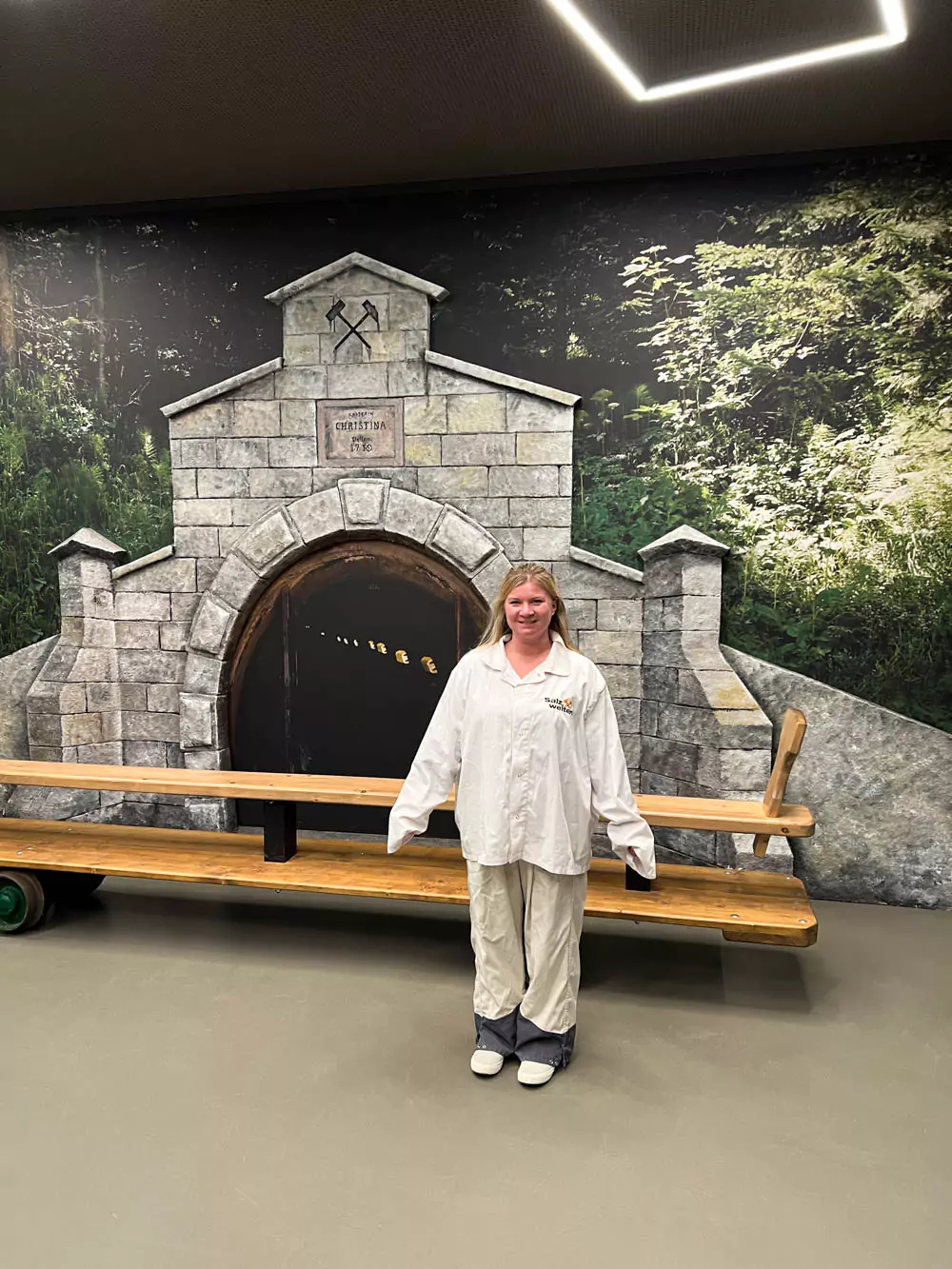 Katie wearing the white miner’s outfit provided at the Hallstatt Salt Mine (Salzwelten), including a zip-up top and pants, standing inside the mine. Her protective gear reflects the traditional uniform worn during the guided underground tours.