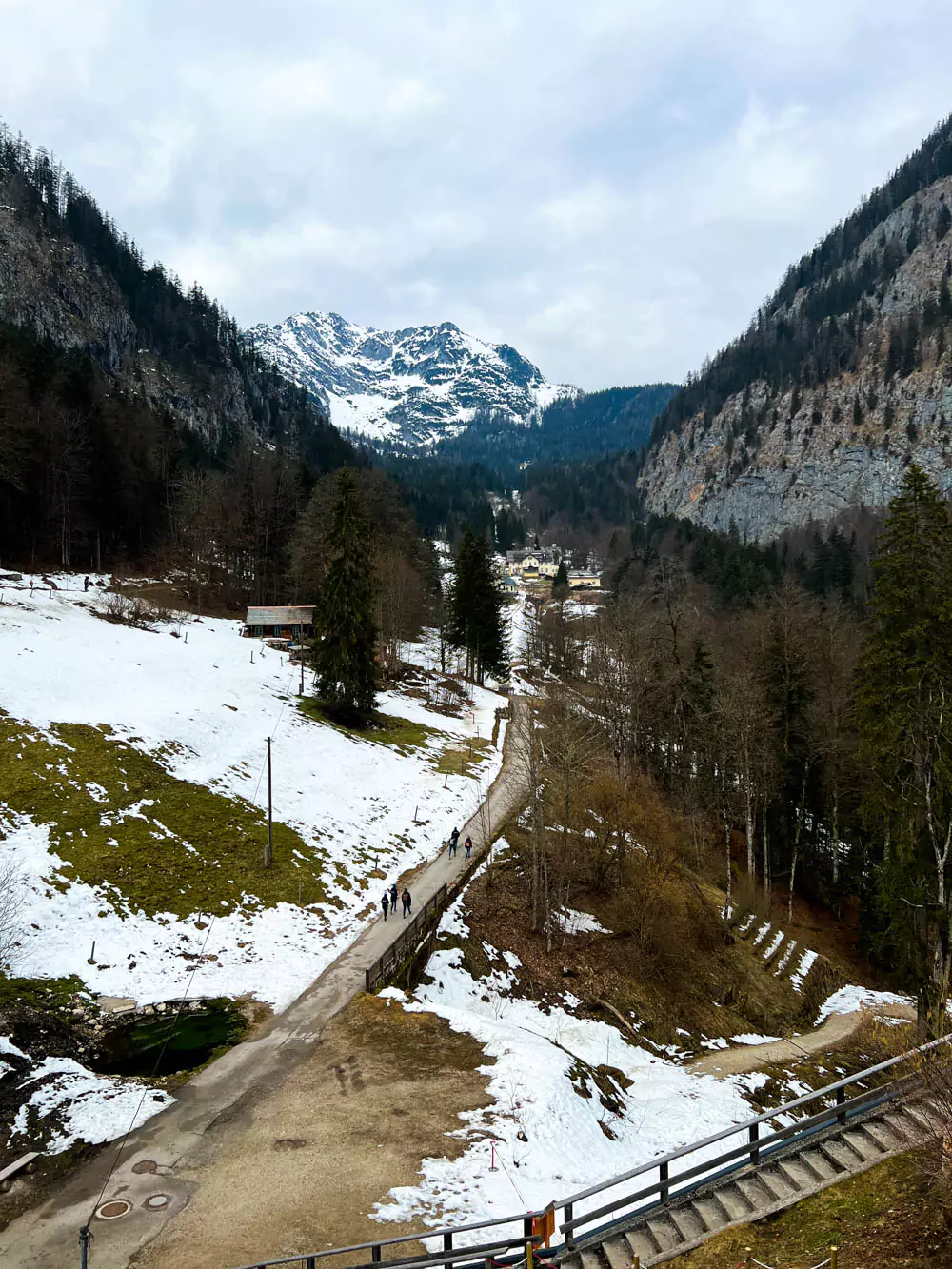 Snow-covered path leading through the Hallstatt Salt Mine (Salzwelten) area in winter, bordered by trees dusted with snow and rustic wooden railings. The trail winds gently through the alpine landscape, creating a peaceful and frosty atmosphere.