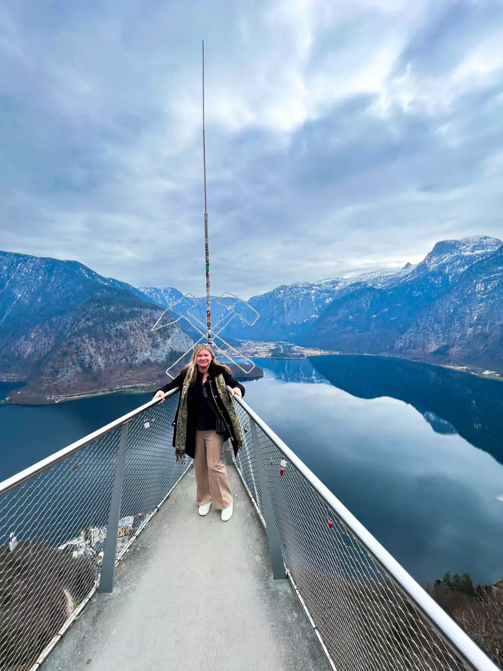 Katie standing on the Welterbeblick World Heritage Skywalk platform at Hallstatt Salt Mine (Salzwelten), with expansive views of Hallstatt village, Hallstätter See, and the surrounding alpine peaks behind her. The glass platform offers a thrilling and scenic perspective high above the valley.