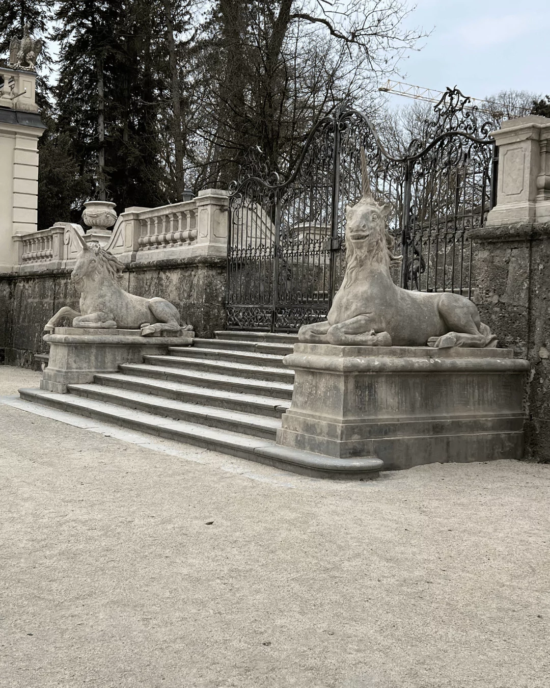 Stone staircase in the gardens of Schloss Mirabell, flanked by two baroque statues on pedestals, leading up through manicured greenery in the heart of Salzburg, Austria.