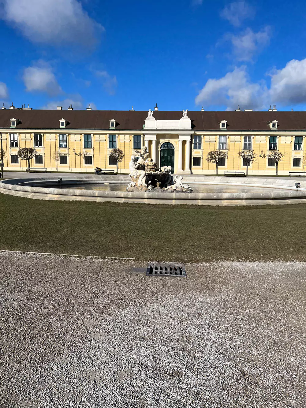 Fountain in the courtyard entrance of Schönbrunn Palace in Vienna, Austria, featuring sculpted marble figures and flowing water, set against the grand yellow façade of the historic Baroque residence.