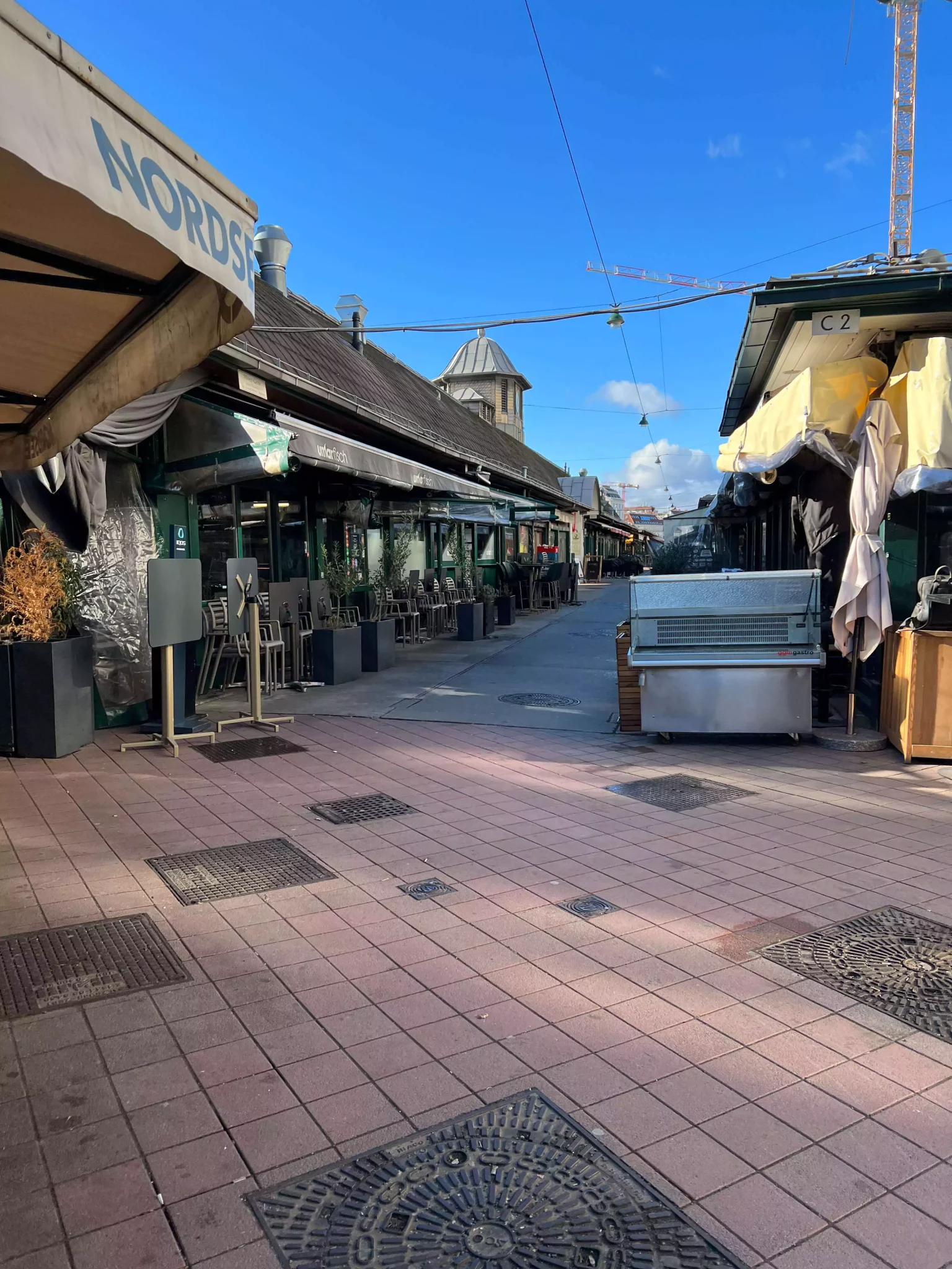 Vienna’s Naschmarkt in the morning, with market stalls just opening, vendors arranging fresh produce, spices, and international delicacies along a wide walkway, set against the backdrop of historic buildings.