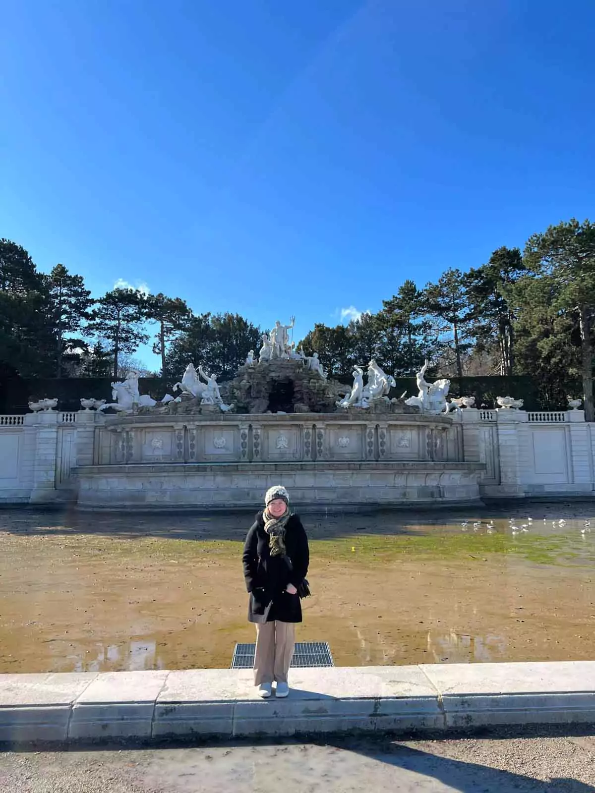 Katie standing in front of the Neptune Fountain at Schönbrunn Palace in Vienna, Austria, with baroque sculptures and cascading water behind her