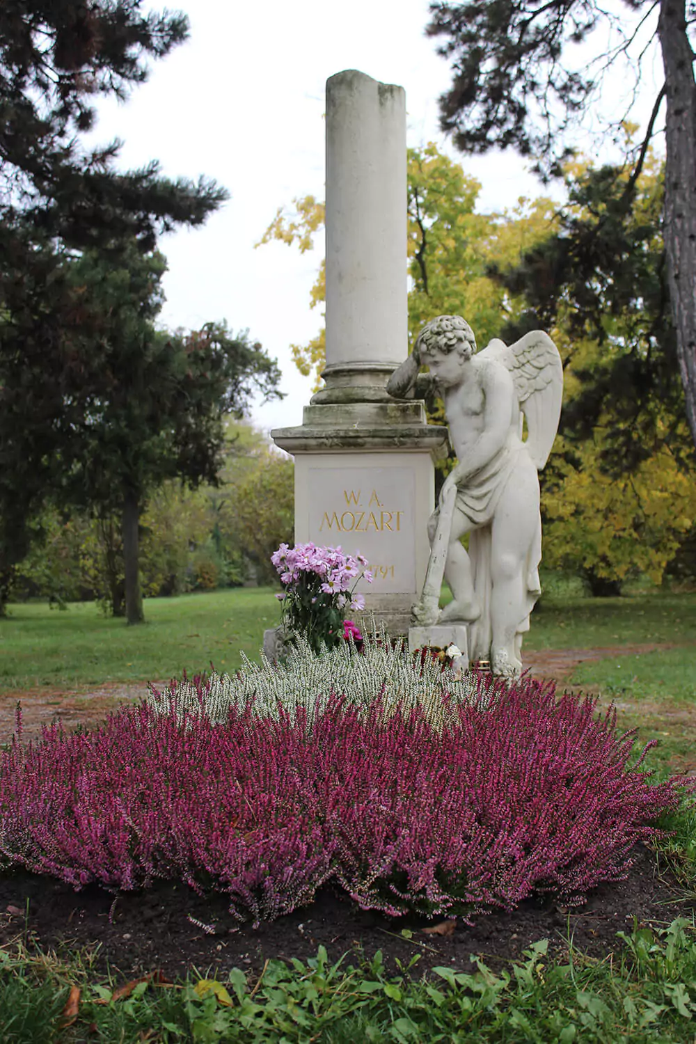 Mozart’s grave at St. Marx Cemetery in Vienna, Austria, marked by a white monument surrounded by flowers and greenery, honoring the composer in the peaceful, historic burial ground where he was laid to rest.