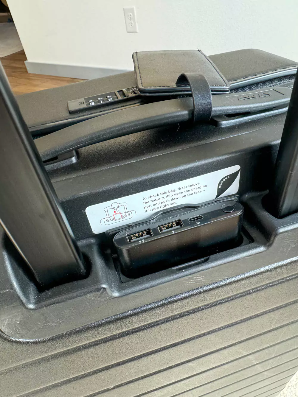 Battery pack charger included with the AWAY Bigger Carry-On Suitcase, shown partially removed from its built-in compartment near the handle — a smart travel feature