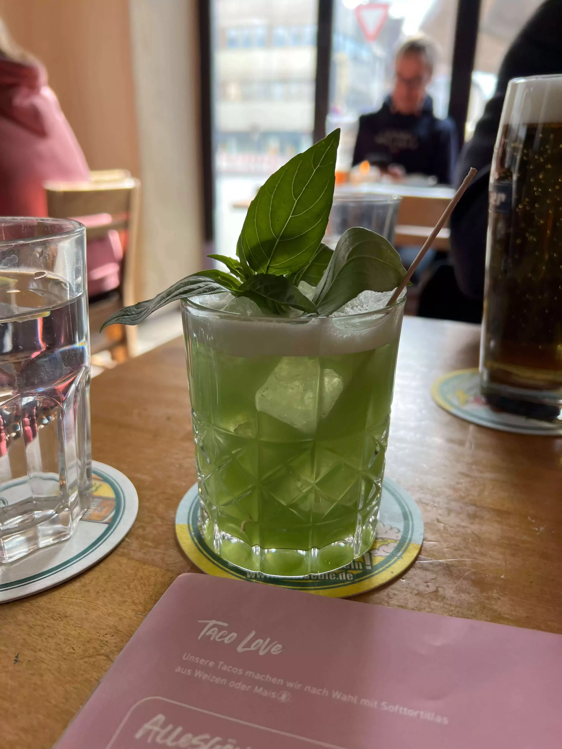 Refreshing Basil Smash cocktail served at Sausalitos in Nuremberg, Germany, featuring a vibrant green hue, fresh basil leaves, crushed ice, and a citrusy gin base in a chilled glass.