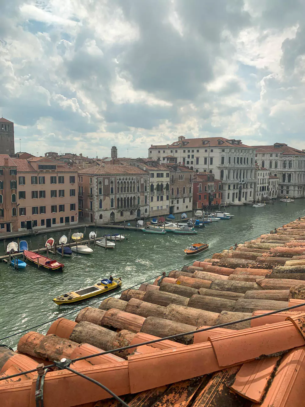 Stunning view of the Grand Canal in Venice, Italy, from a terracotta-tiled rooftop, with boats drifting along the turquoise water, historic buildings lining the canal, and soft golden light illuminating the scene.