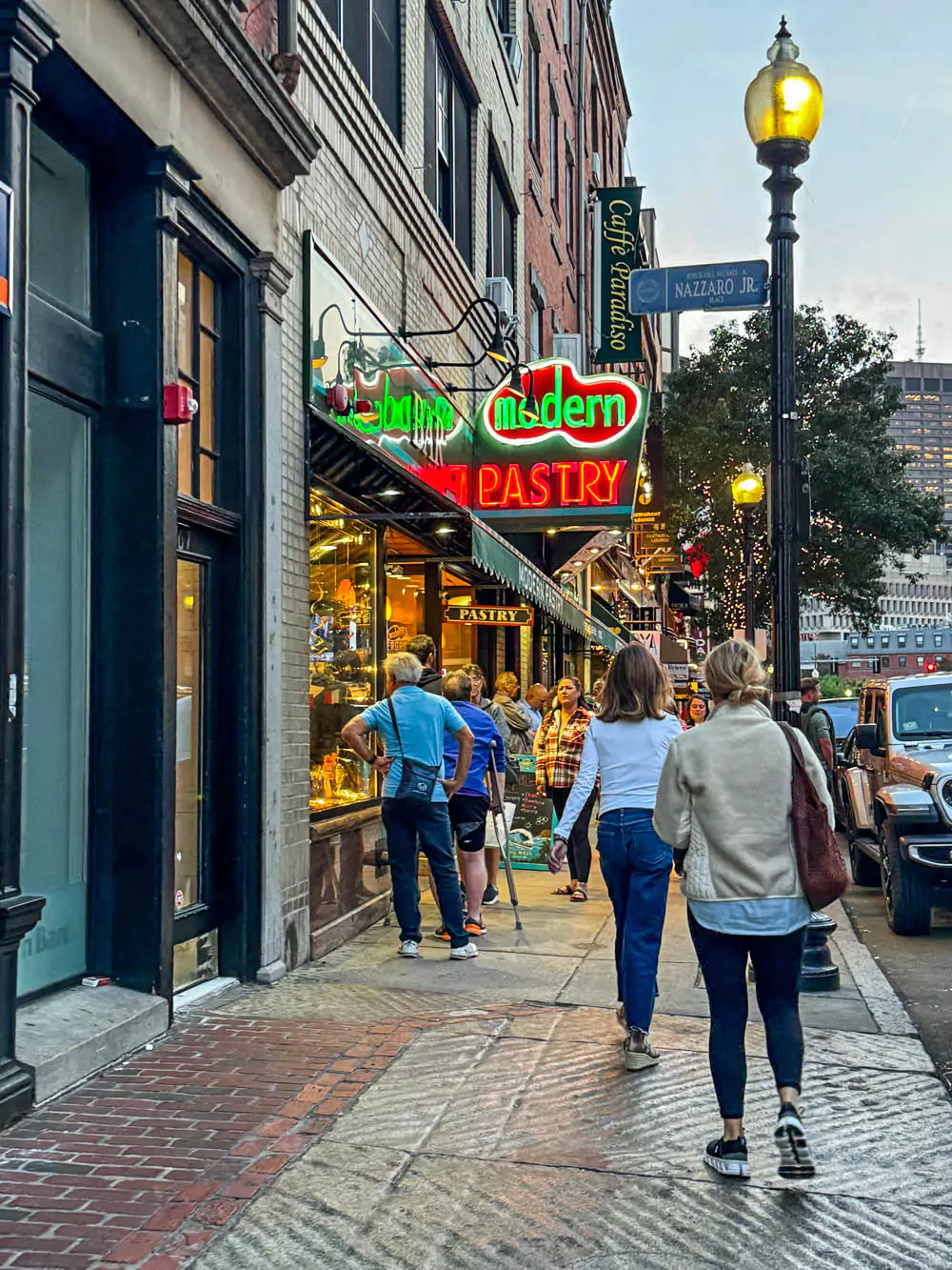 The vibrant entrance of Modern Pastry in Boston’s North End, featuring a colorful awning and a display window filled with Italian pastries. The historic brick building and busy sidewalk highlight the bakery’s popular spot in the neighborhood.