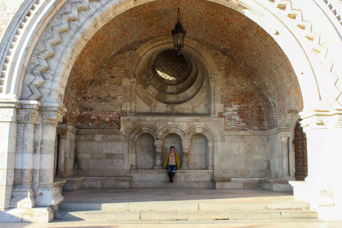 Katie sits relaxed beneath a stone archway at Fisherman’s Bastion in Budapest, framed by the historic terrace’s ornate architecture. The view hints at the cityscape beyond, blending a moment of calm with the landmark’s medieval charm.