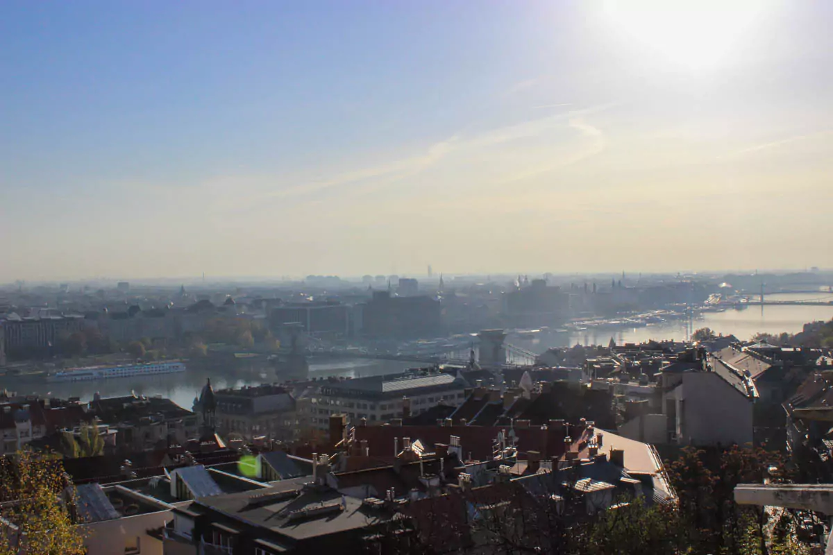 Panoramic view of Budapest bathed in soft morning light, showcasing the Danube River, historic bridges, and grand architecture of the city. The warm glow highlights landmarks like the Parliament building and Buda Castle against a clear sky.
