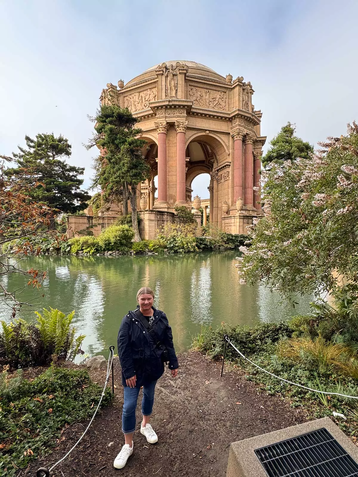 Katie standing in front of the grand rotunda at the Palace of Fine Arts in San Francisco, with its towering columns and ornate dome. The elegant classical architecture and reflective lagoon create a picturesque, tranquil backdrop.