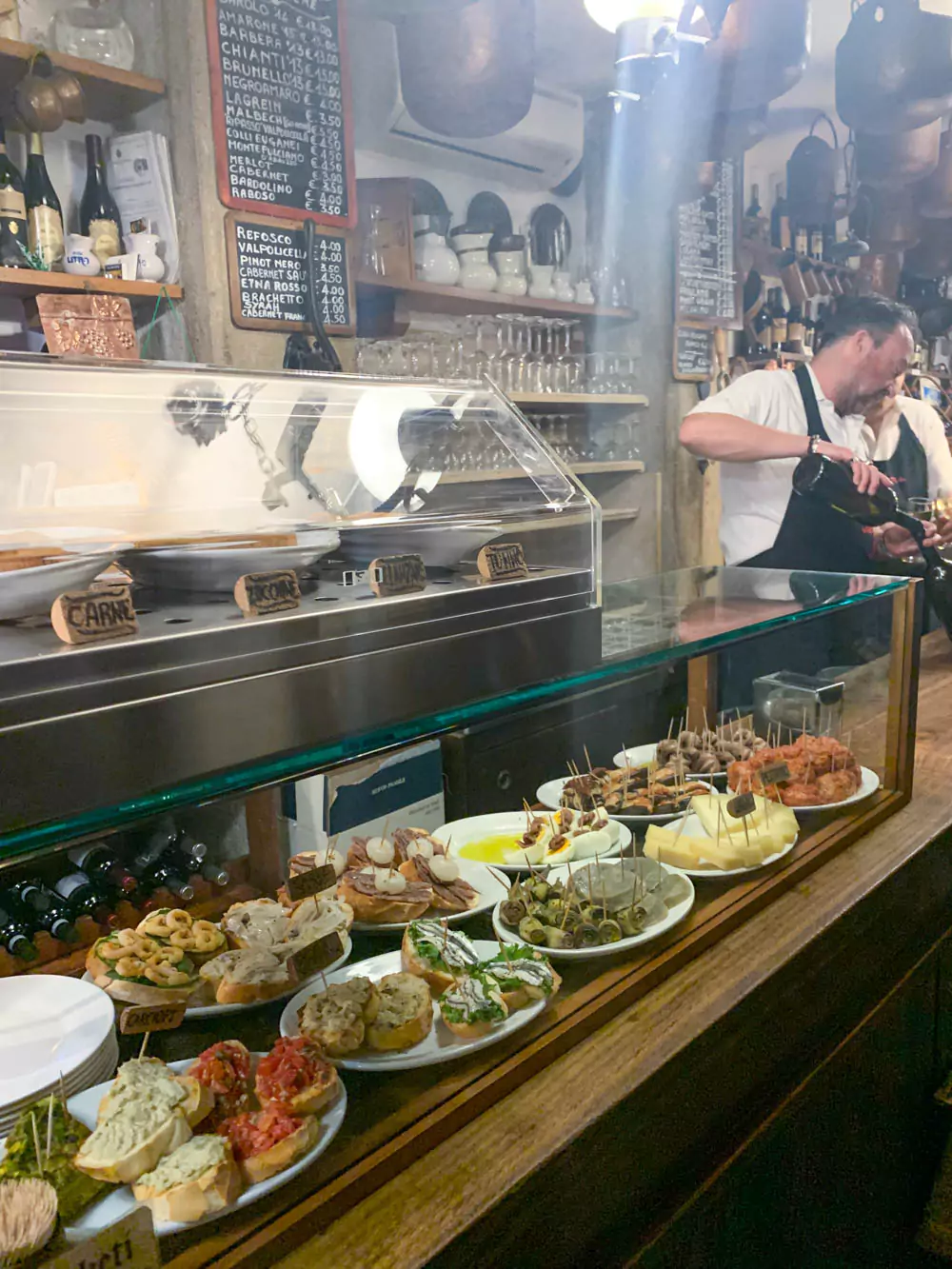 Traditional cicchetti served at Cantina Do Mori in Venice, Italy, featuring a variety of small bites like crostini, cured meats, seafood, and marinated vegetables on rustic wooden counters in a historic wine bar setting.