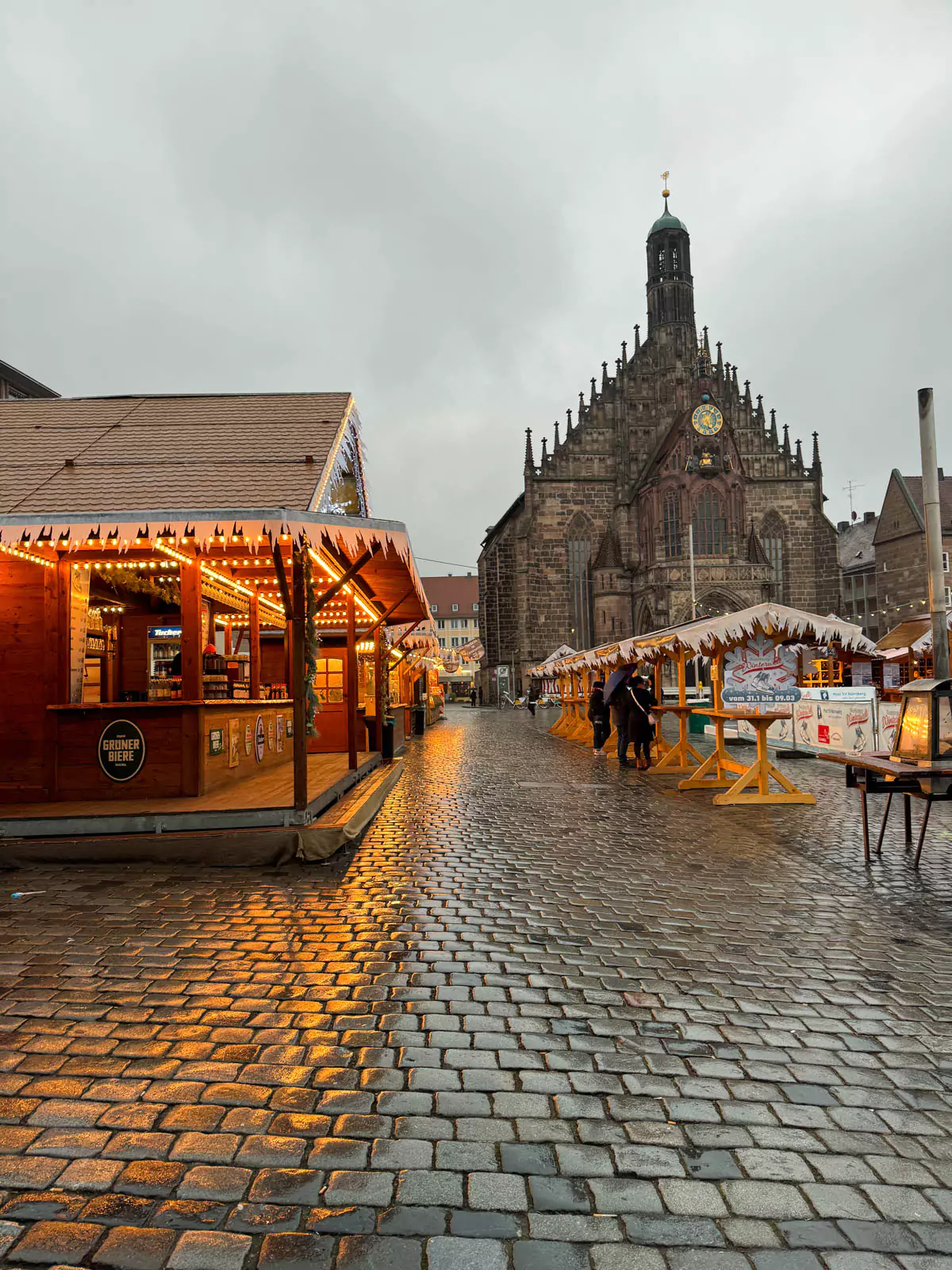 Nuremberg Christkindlesmarkt, a festive Christmas market filled with red-and-white striped stalls, twinkling lights, and holiday decorations. Crowds browse handcrafted gifts and seasonal treats beneath the backdrop of historic buildings and a glowing tree.