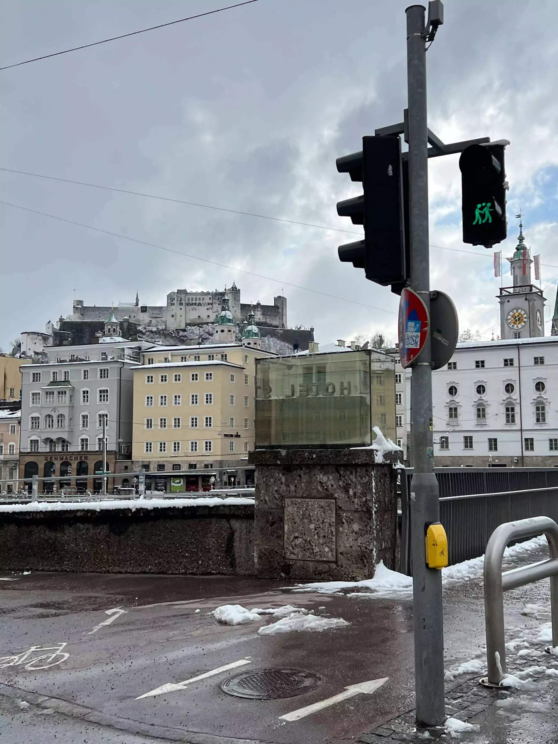 A cute street crossing sign in Salzburg’s Old Town shows two stylized figures holding hands, one slightly taller than the other. The charming design adds a playful, human touch to the historic city’s pedestrian pathways.