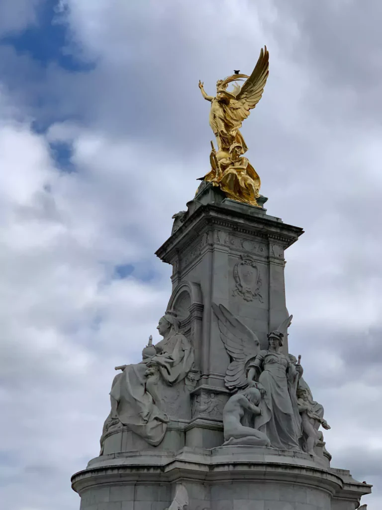 Queen Victoria Memorial in front of Buckingham Palace in London, England, featuring the grand white marble monument topped with a golden statue. The palace’s iconic facade provides a royal backdrop, drawing visitors to this historic ceremonial site.