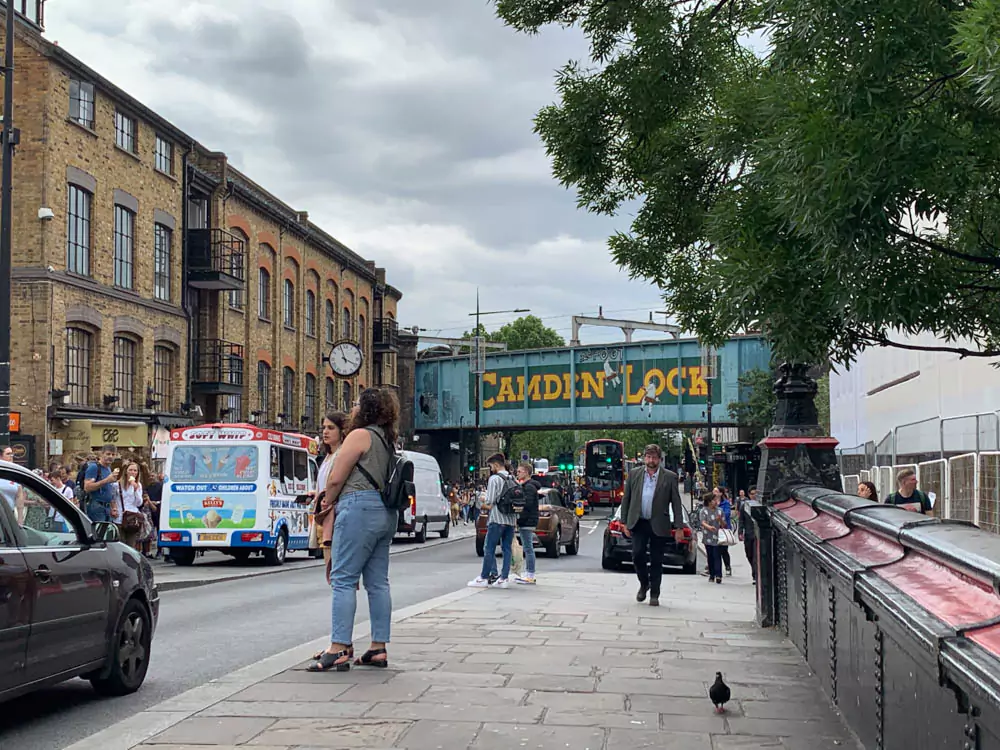 Bustling scene at Camden Market in London, with colorful storefronts, eclectic food stalls, and crowds exploring the vibrant marketplace. The area’s creative, alternative vibe is reflected in bold signage and artistic street details.