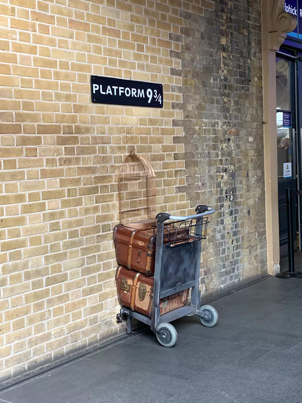 King’s Cross Station in London with the famous Platform 9¾ photo spot, featuring a luggage trolley embedded in the wall beneath a sign marked “Platform 9¾.” Fans gather to take photos, celebrating the magical gateway from the Harry Potter series.