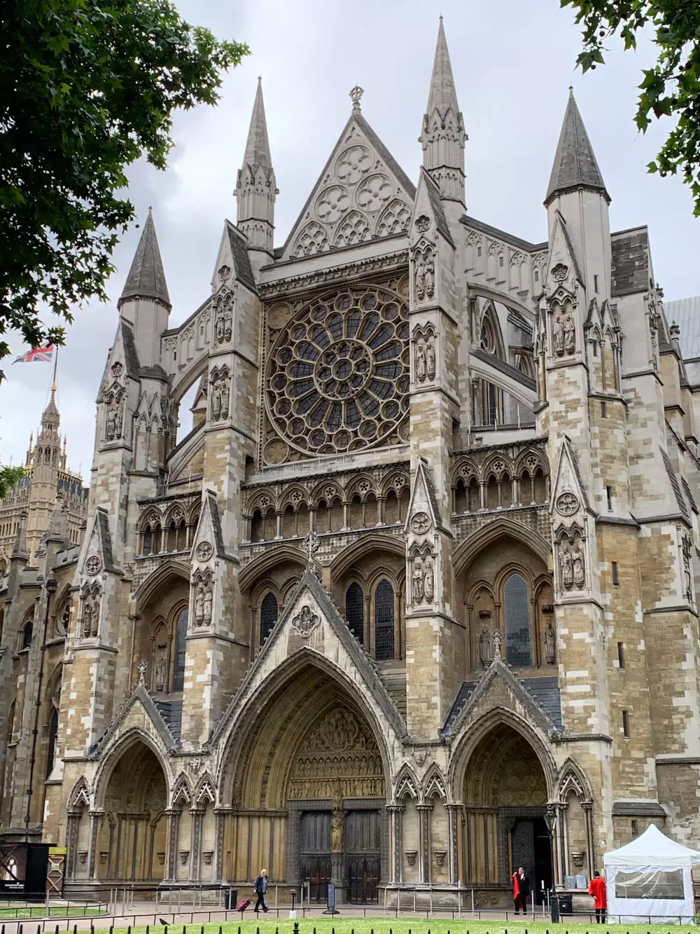 Exterior of Westminster Abbey in London, showcasing its grand Gothic architecture, pointed arches, intricate stone carvings, and tall towers under a bright sky.