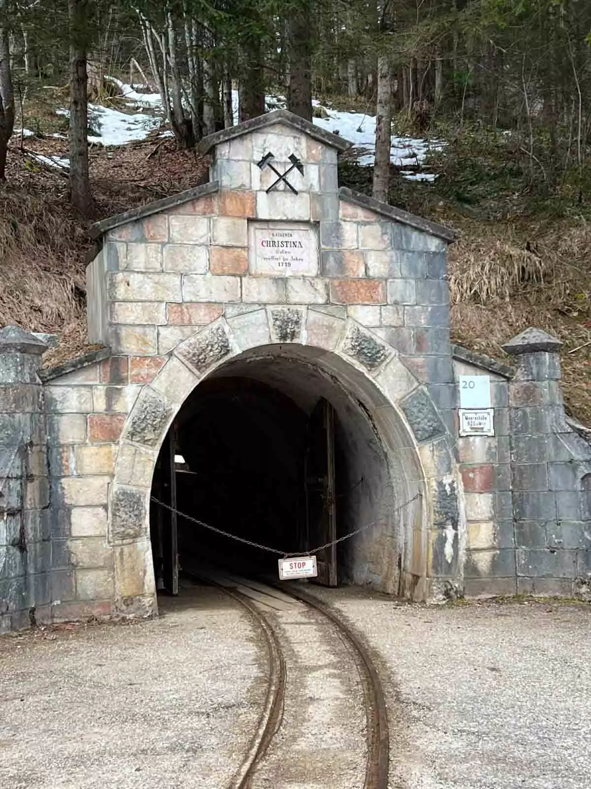 Entrance to the Salt Mine Christina at Hallstatt, Austria, featuring a wooden mine tunnel framed by rocky hills and surrounded by alpine forest, marking the start of the underground tour.