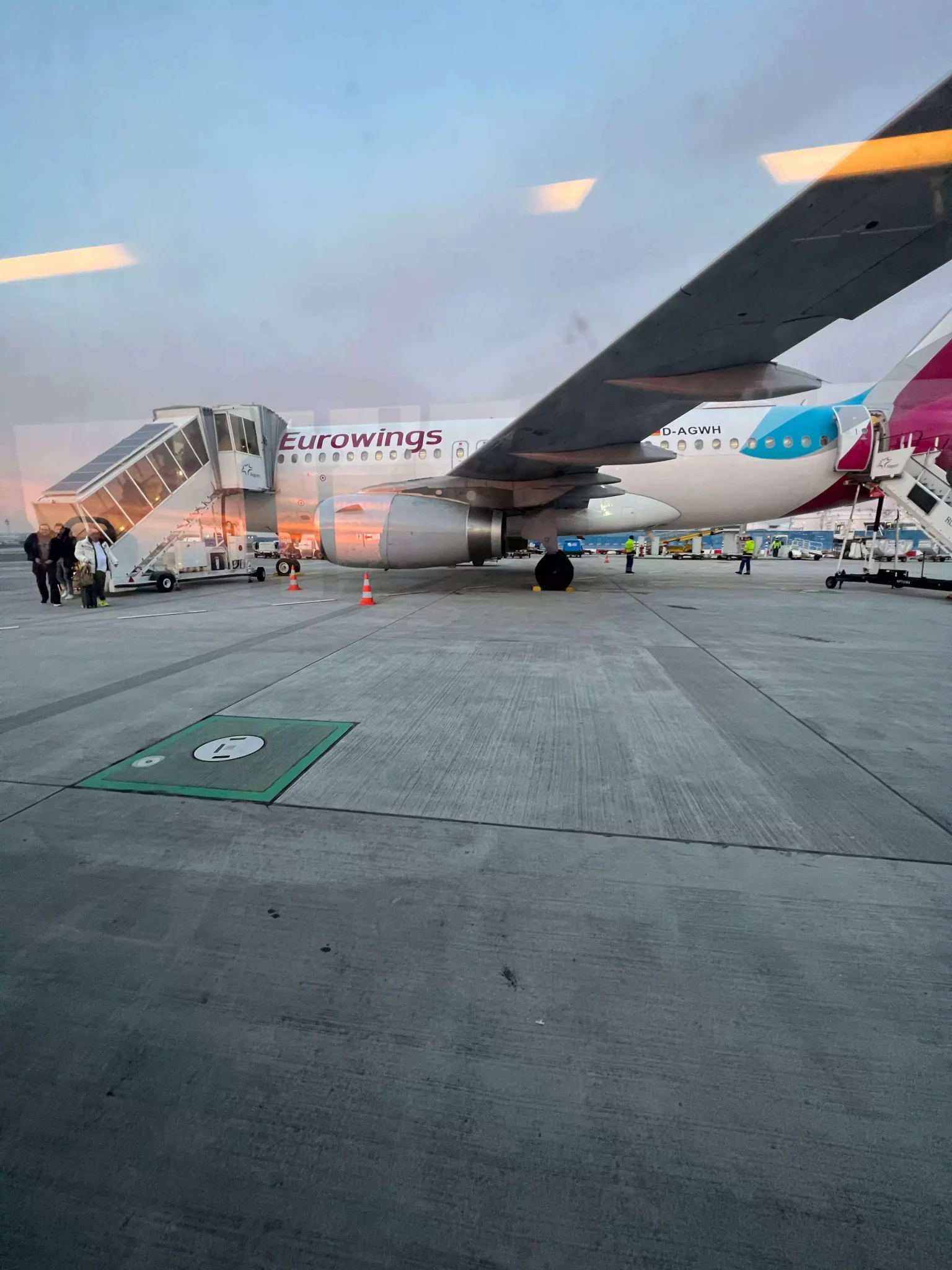 A Eurowings airplane sits on the tarmac at Frankfurt Airport in Germany, with ground service vehicles nearby and the terminal visible in the background. The aircraft’s sleek white and maroon design stands out under a cloudy European sky.