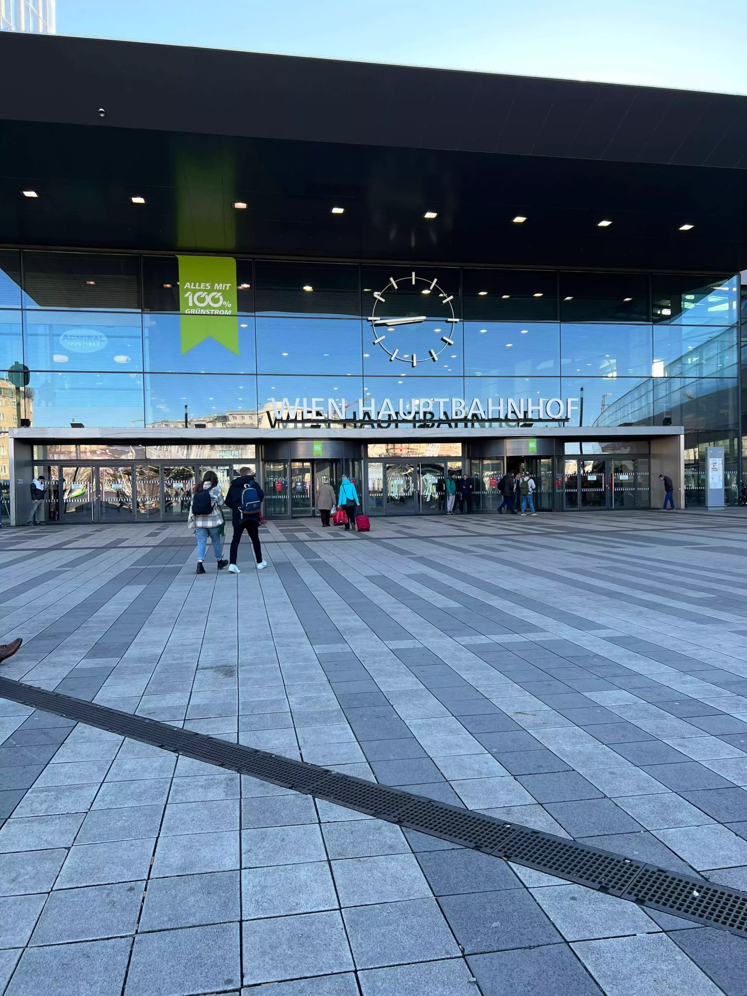 The exterior of Wien Hauptbahnhof, Vienna’s central train station, features a sleek, modern design with a wide glass entrance and bold signage. Travelers move in and out of the busy plaza, highlighting the station’s role as a major transportation hub.