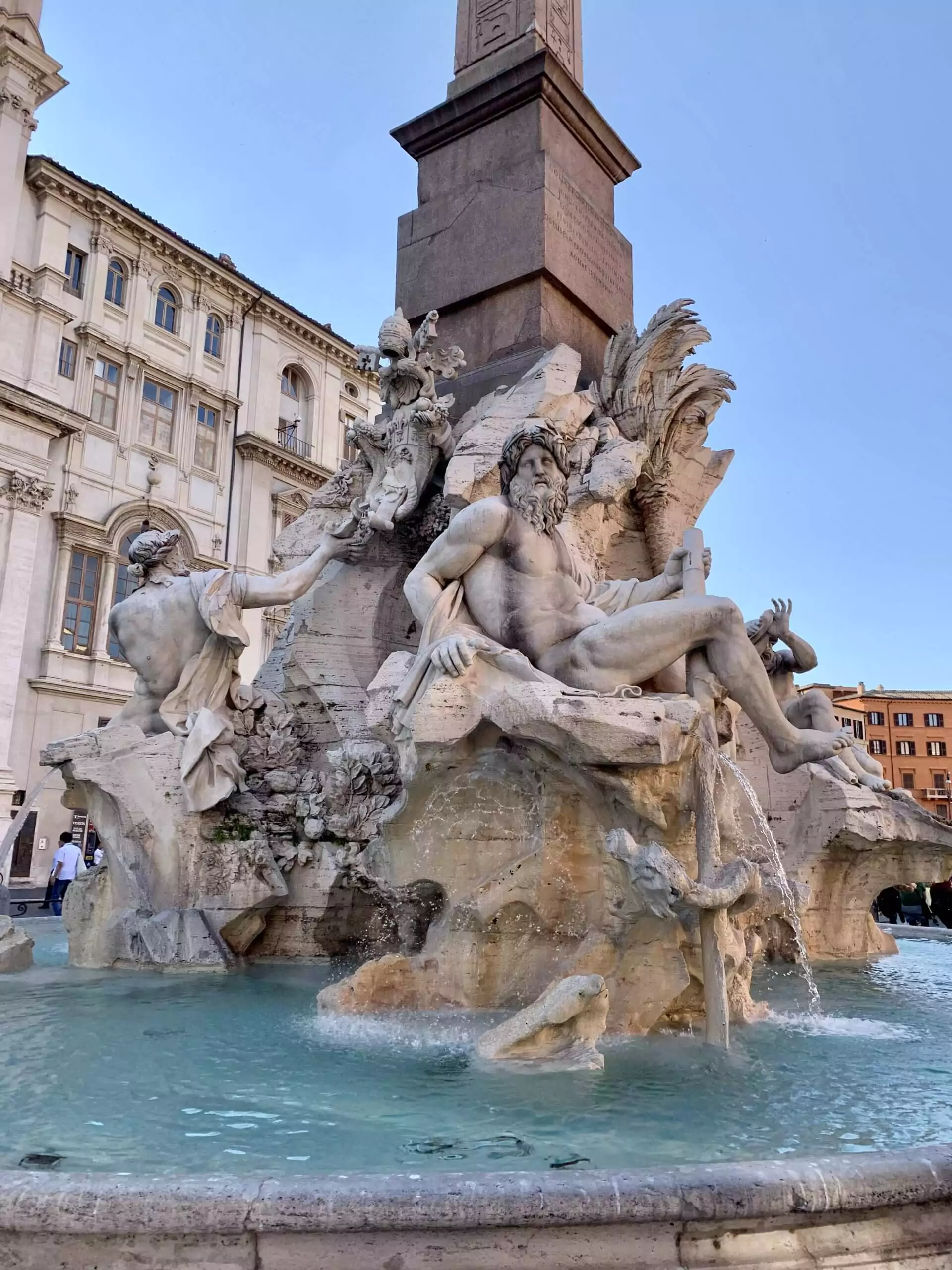 The Fiumi Fountain in Piazza Navona, Rome, featuring dramatic marble sculptures representing four major rivers, set around a central obelisk with water cascading into a large basin.