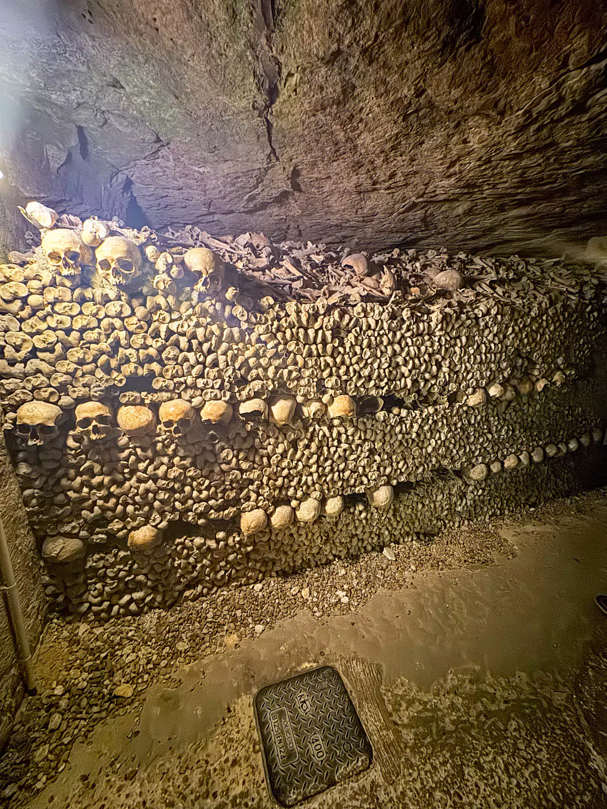 Walls of human bones and skulls stacked in the ossuary of the catacombs, arranged in precise, layered patterns along the dimly lit stone corridor, reflecting centuries of burial tradition.