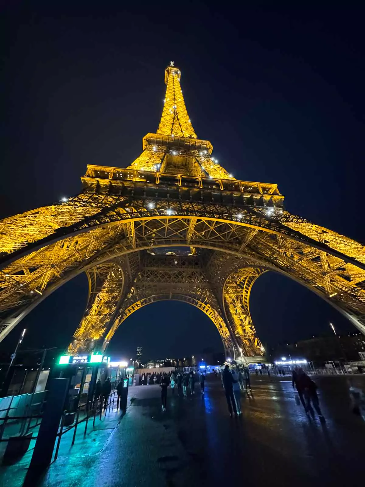 The Eiffel Tower at night in Paris, France, glowing with golden lights against the dark sky, its beacon shining from the top and casting a magical glow over the city — a dazzling view