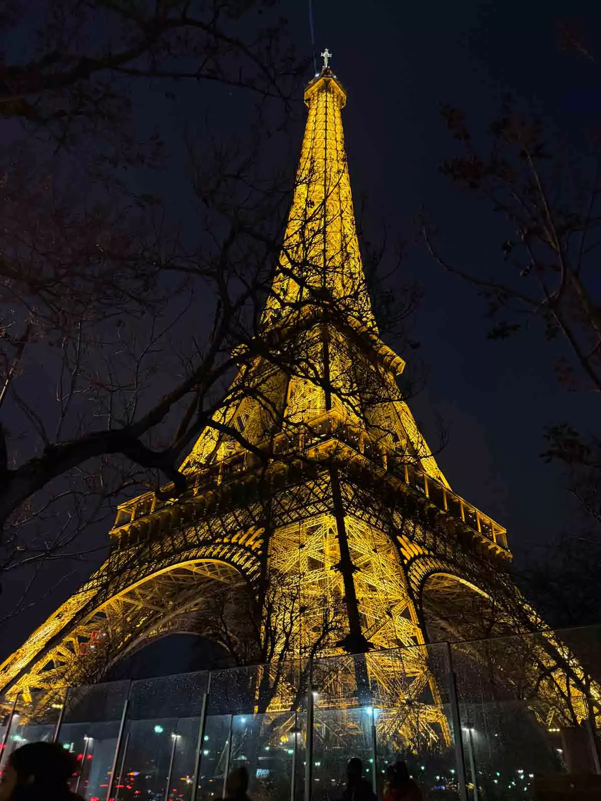 The Eiffel Tower at night in Paris, France, glowing with golden lights against the dark sky, its beacon shining from the top and casting a magical glow over the city — a dazzling view
